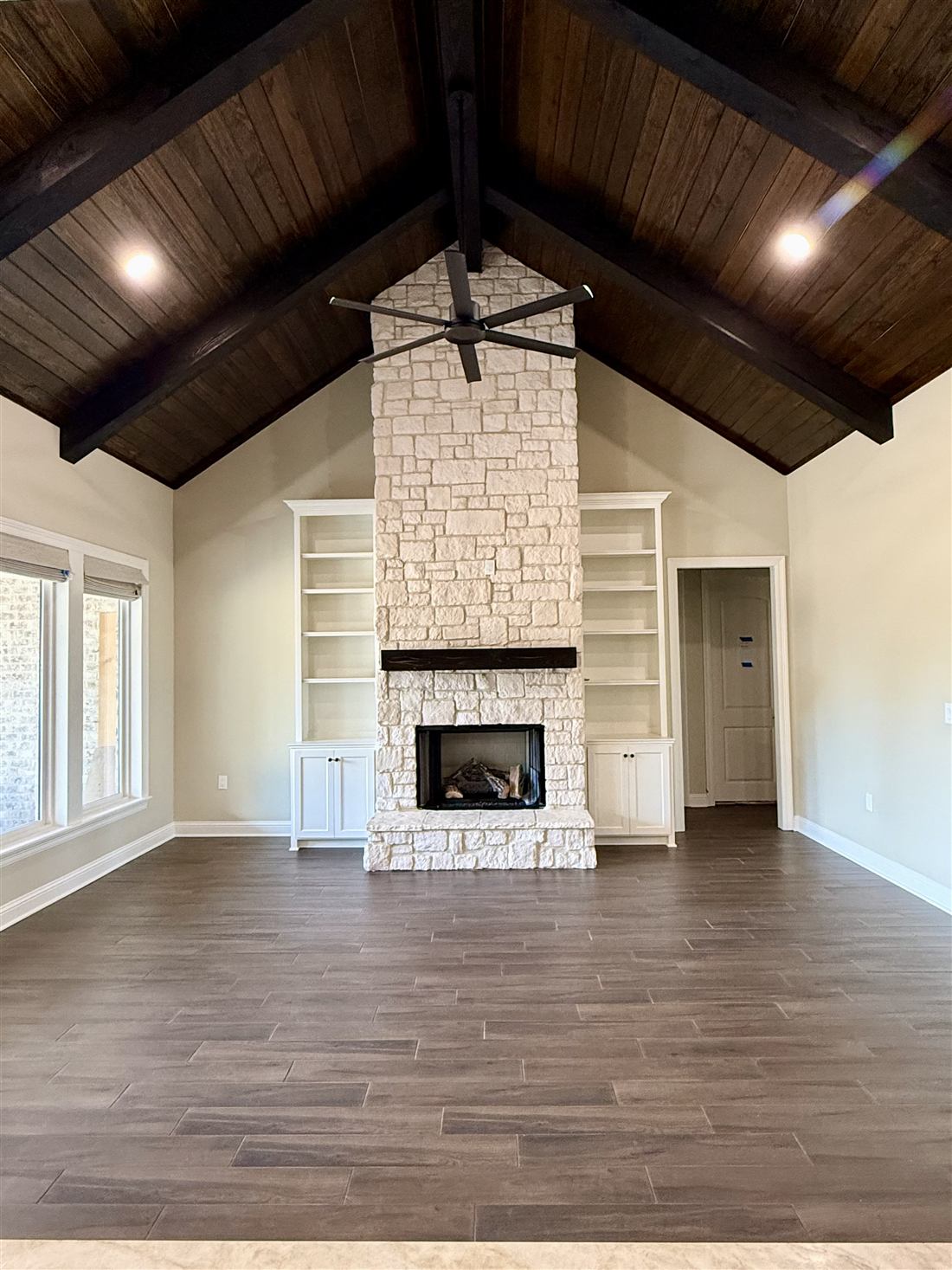 Great room with vaulted dark wood ceiling, exposed beams and white stone fireplace with built-ins