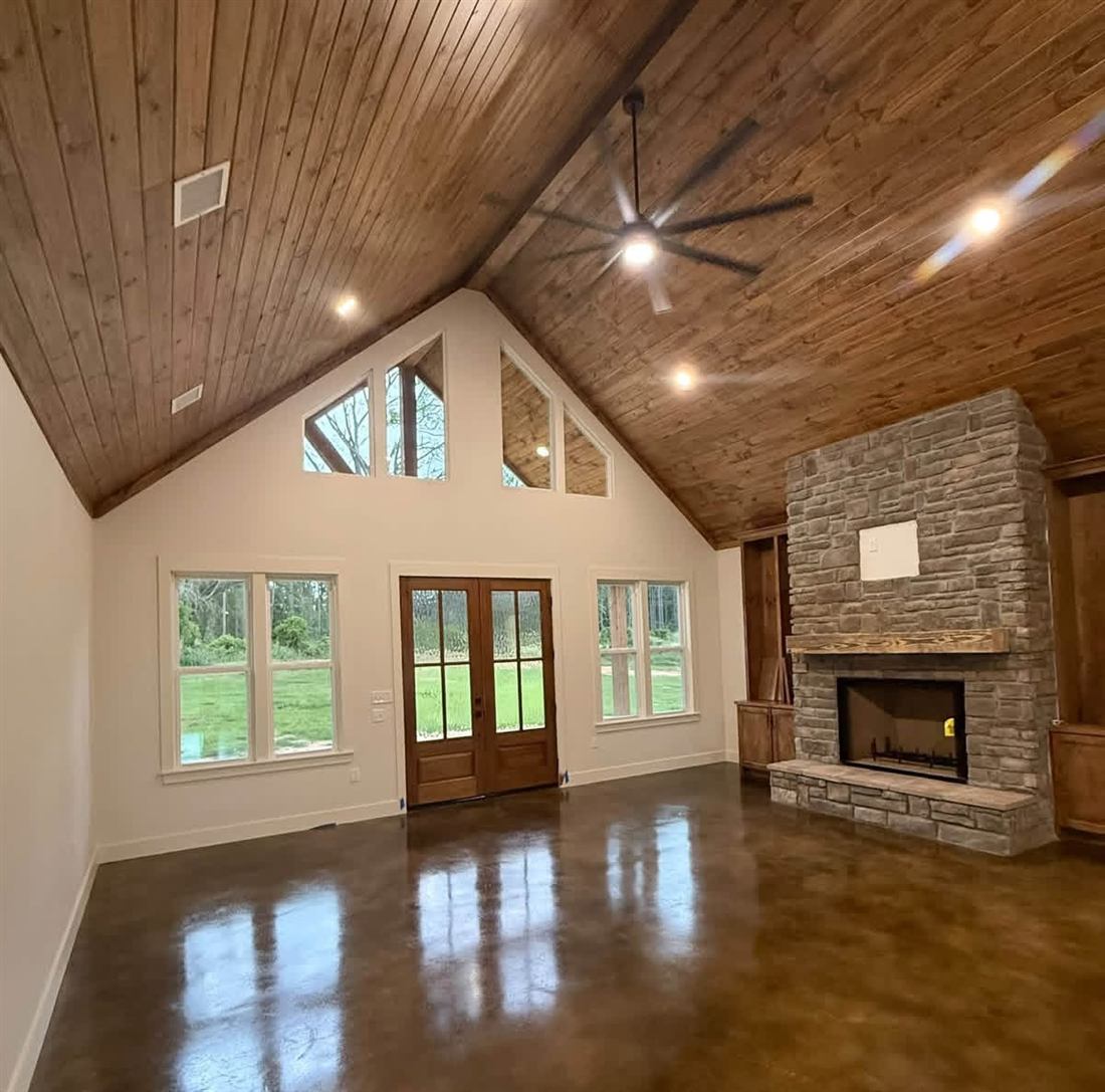 Vaulted wood ceiling great room with stone fireplace and stained concrete floors in a custom built home