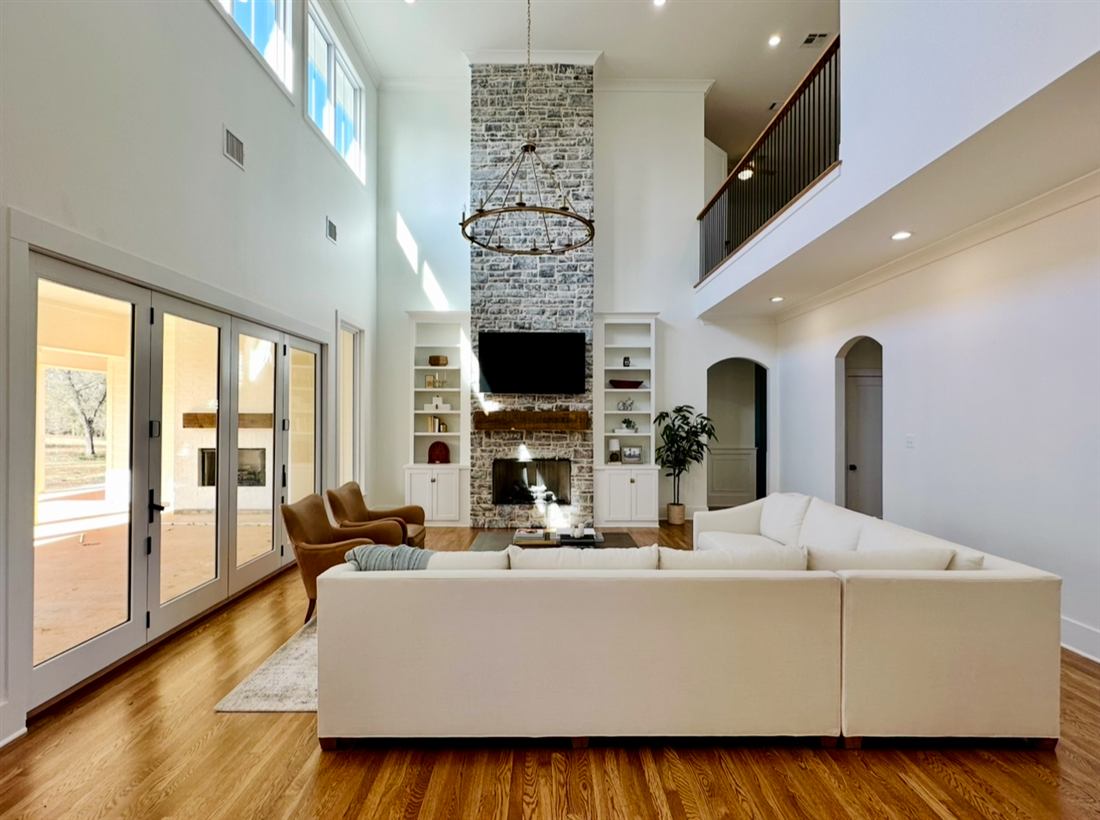Two-story living room with stone fireplace, chandelier and custom built-ins in a new construction home